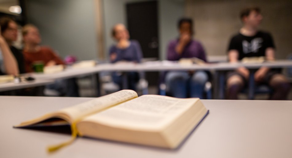 Oppslått bok i seminarrom med studenter