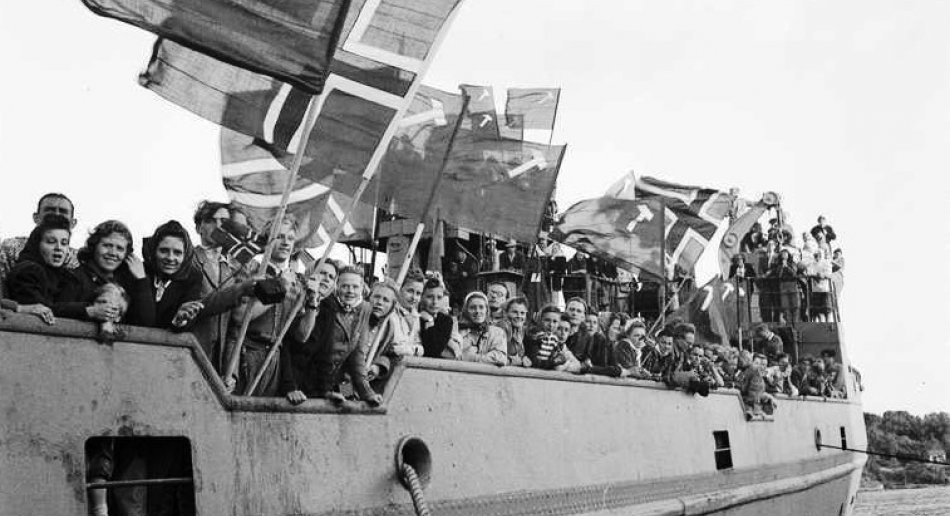 Historisk bilde av Arbeidernes Ungdomsfylking på vei til leir i Danmark med M/S Svalbard, med norske flagg og kommunistflagg.