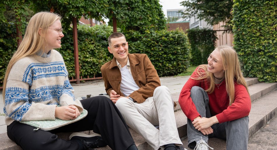 Tre studenter som sitter i en trapp ute.